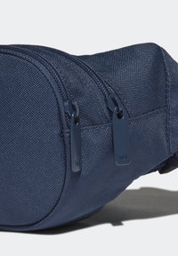 Námořnická modrá ledvinka s texturovaným povrchem, která má dvě zipové kapsy a tmavě modré zipy s detaily loga.