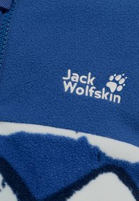 Μπλε ύφασμα φλις με λευκό κεντημένο λογότυπο Jack Wolfskin και πατουσίδα κοντά σε μπλε φερμουάρ.