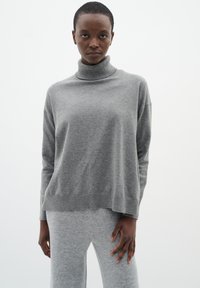 Gray knit turtleneck sweater with a relaxed silhouette and ribbed hem, paired with matching gray knit pants. Soft texture throughout.