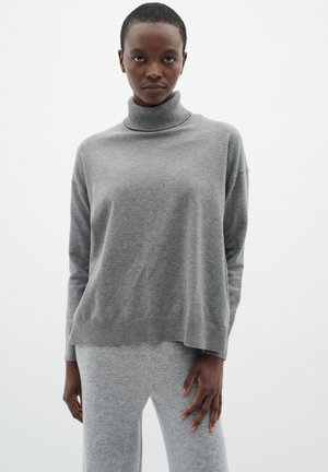Gray knit turtleneck sweater with a relaxed silhouette and ribbed hem, paired with matching gray knit pants. Soft texture throughout.