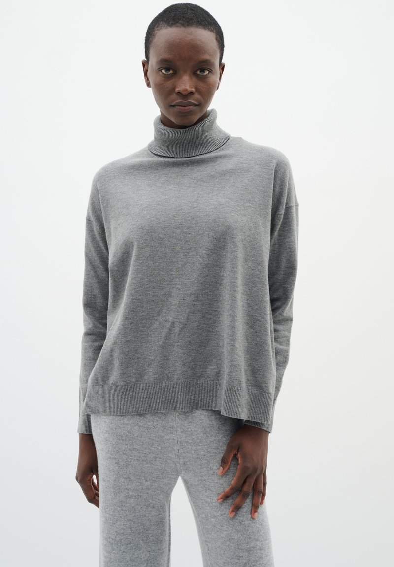 Gray knit turtleneck sweater with a relaxed silhouette and ribbed hem, paired with matching gray knit pants. Soft texture throughout.
