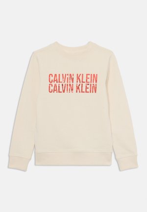 Beige hettegenser med rund hals og lange ermer. Framsiden viser gjentatt "CALVIN KLEIN" tekst i rød, med en litt slitt finish.