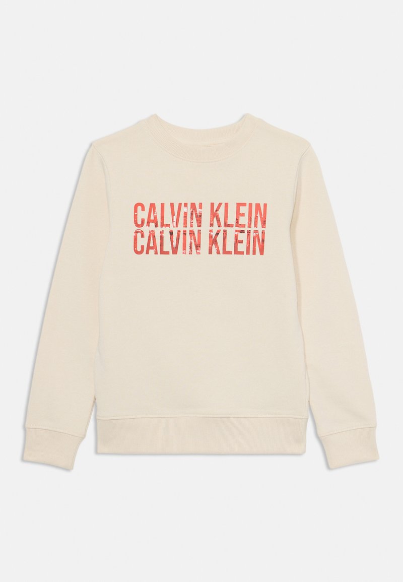 Béžová mikina s okrúhlym výstrihom a dlhými rukávmi. Na prednej strane sa opakuje text "CALVIN KLEIN" v červenej farbe s mierne ošúchaným vzhľadom.