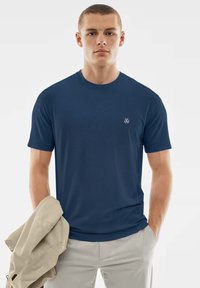 Dunkelblaues T-Shirt mit kurzen Ärmeln und Rundhalsausschnitt, mit einem kleinen weißen Logo auf der Brust. Weiche, glatte Stoffstruktur.