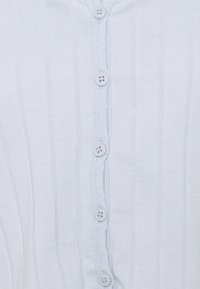 Světle modrý žebrovaný kardigan s knoflíkovou výbavou vpředu. Má šest bílých knoflíků uprostřed a je z měkké, texturované elastické tkaniny.