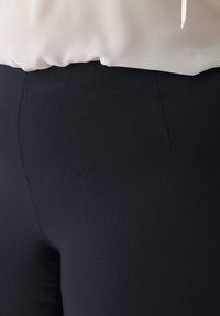 Schwarze Stretchhose mit glatter Textur, ausgestattet mit einem schmalen Bund und minimalen Nahtdetails. Der Stoff wirkt weich und figurbetont.