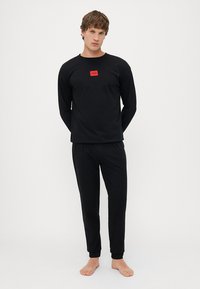 Conjunto de camiseta de manga larga y pantalones negros, con un pequeño logo rojo en el pecho. Fabricado con un tejido suave y elástico, con un diseño ajustado.