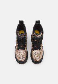 Botines de tobillo negro y dorado con purpurina, cordones negros, suelas de goma y forro interior amarillo. Presentan una etiqueta con el logo en la lengüeta.