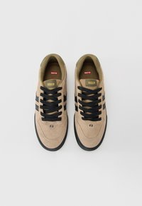 Pár béžových semišových tenisek s černými pruhy a tkaničkami, označených "Globe," pohledem shora na bílém pozadí.