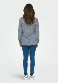 Cămașă cu dungi albastre și albe, cu un croi lejer, mâneci lungi și tiv rotunjit. Este asociată cu blugi skinny albaștri și adidași albi.
