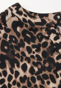 Il tessuto a stampa leopardata presenta diverse tonalità di marrone e nero, con una texture liscia e un collo a giro. Cuciture decorative visibili al colletto.