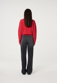 Roter Strickpullover, weite schwarze Jeans mit hoher Taille und Gesäßtaschen, von hinten auf einem schlichten weißen Hintergrund betrachtet.