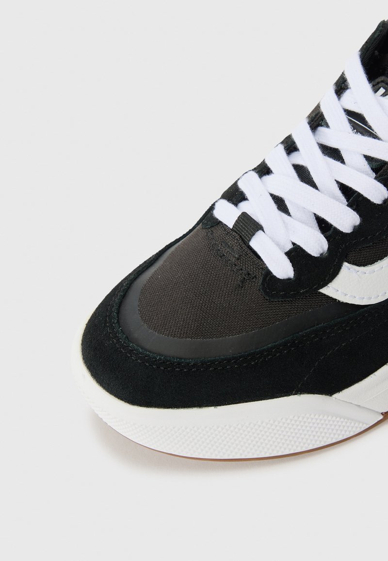 Schwarzer Sport-Schuh aus Wildleder und Stoff, mit weißen Schnürsenkeln, einer strukturierten Sohle und einem schlanken Design mit einem weißen Logo-Akzent.