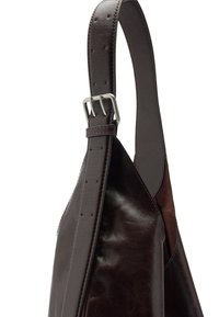Brązowa skórzana torba o gładkim wykończeniu, z szerokim paskiem na ramię, metalową klamrą i miękkimi zamszowymi akcentami. Kształt jest trójkątny.