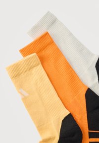 Τρία ζευγάρια ραβδωτές κάλτσες πλήρους μήκους σε ανοιχτό κίτρινο, λαμπερό πορτοκαλί και ανοιχτό γκρι με μαύρα άκρα σε λευκό φόντο.
