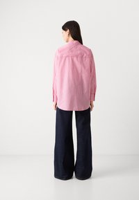 Striped pink shirt with long sleeves, collar, and back yoke detail, paired with wide-leg dark blue denim pants. Back view displayed.