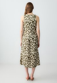 Mouwloze midi jurk in beige stof met groen abstract patroon. A-lijn silhouet met een rechte achterkant en subtiele stikdetails.