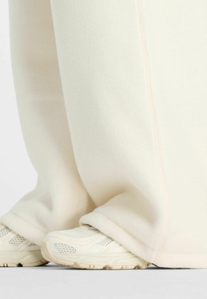 Witte fleecebroek met een zachte textuur, voorzien van een naadloos ontwerp en subtiele roze stiksels, gecombineerd met lichtgekleurde sportschoenen.