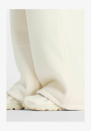 Witte fleecebroek met een zachte textuur, voorzien van een naadloos ontwerp en subtiele roze stiksels, gecombineerd met lichtgekleurde sportschoenen.