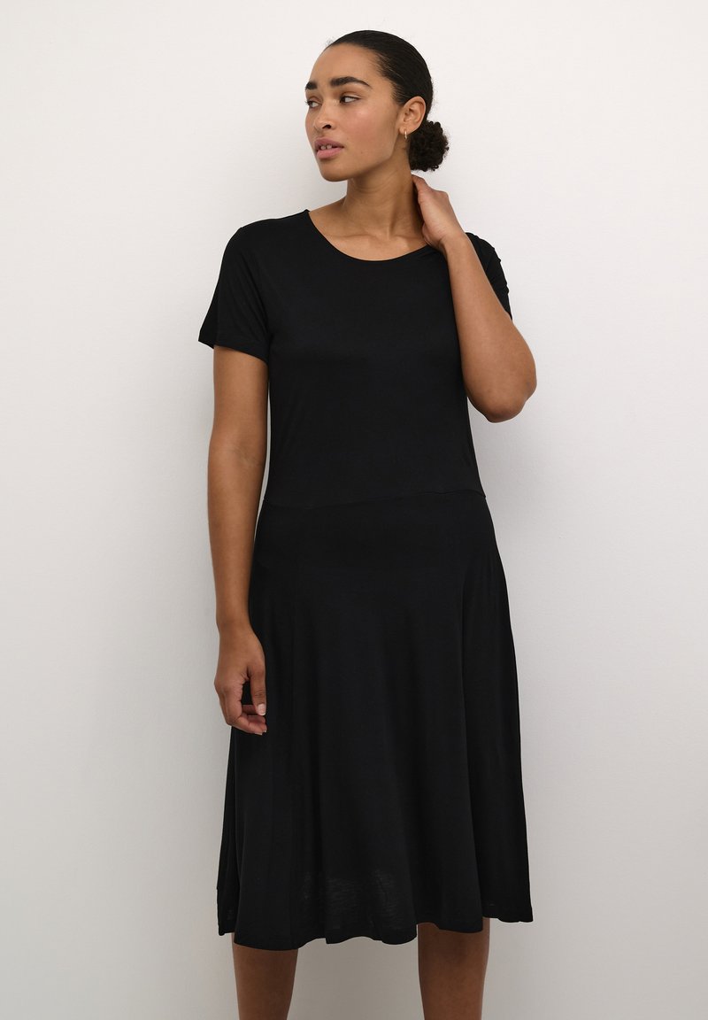 Robe noire en tissu doux, avec un col rond, des manches courtes et une jupe évasée qui arrive au niveau du mollet.