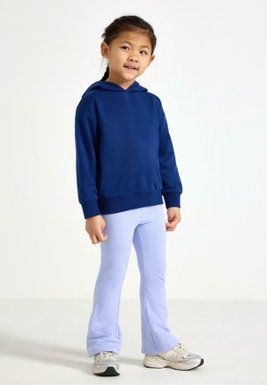 Laivastonsininen huppari kengurutaskulla, yhdistetty vaaleansinisiin liehuviin leggingsseihin. Lapsella on jalassaan harmaat urheilukengät hopeisilla yksityiskohdilla.