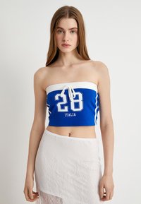Top corto sin tirantes azul con acentos blancos, que presenta el número "28" y la palabra "ITALIA" en letras negritas y de contraste, combinado con una falda blanca de encaje.