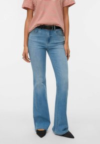 Vaqueros acampanados azul claro hechos de denim, con cintura de talle medio, trabillas para cinturón y detalles descoloridos. Combinados con una camiseta a rayas rojas y tacones negros.