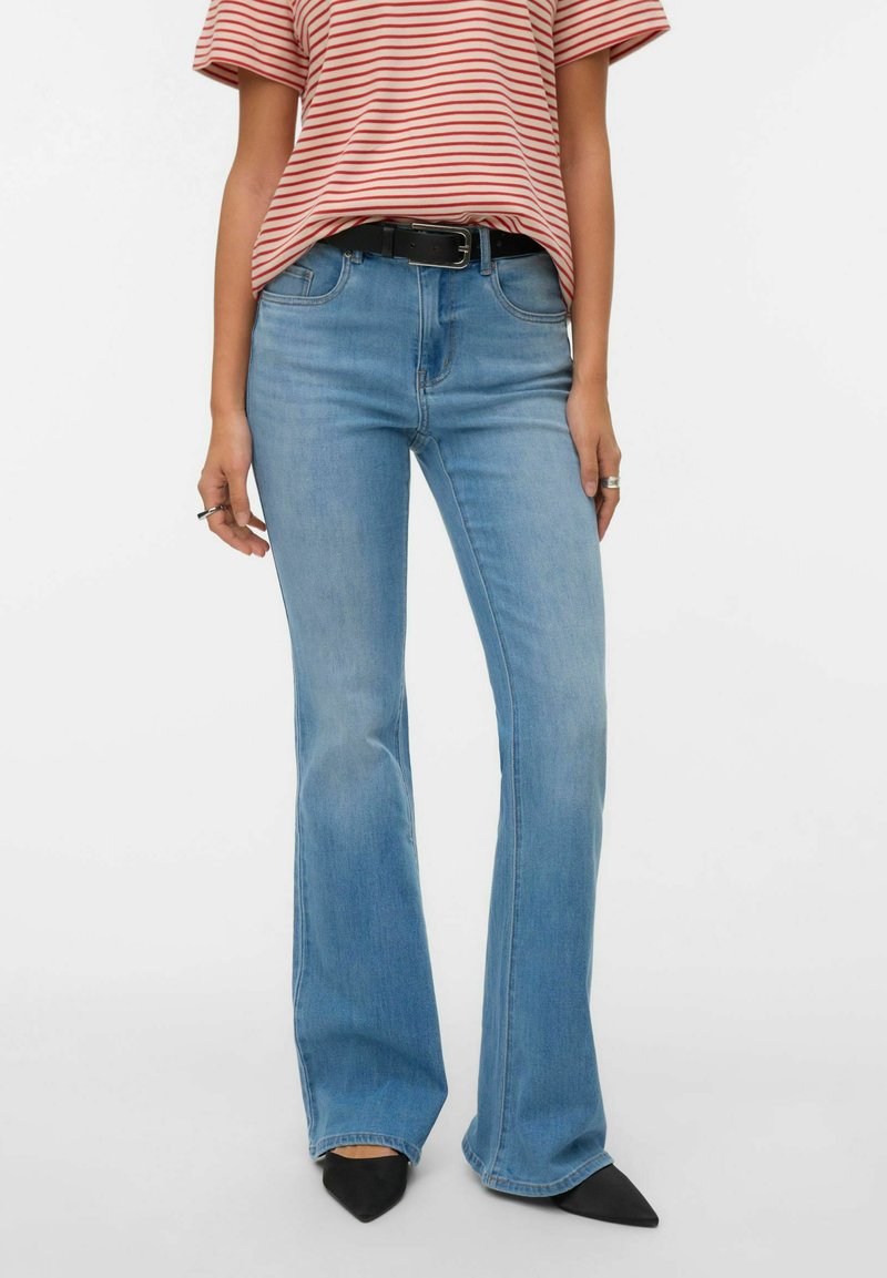 Vaqueros acampanados azul claro hechos de denim, con cintura de talle medio, trabillas para cinturón y detalles descoloridos. Combinados con una camiseta a rayas rojas y tacones negros.