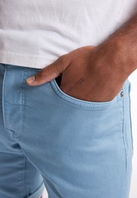 Pantalones cortos de algodón azul claro con una textura suave, que cuentan con un bolsillo lateral y costuras cosidas. Se lleva encima una camiseta blanca.