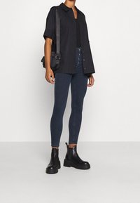 Svart knapp-up skjorta, mörkblå skinny jeans och svarta chunky stövlar. Enkelt mönster, avslappnad passform och jämn textur över hela plagget.