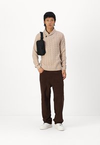 Pull en maille beige clair, pantalon en velours côtelé marron, baskets blanches et petit sac bandoulière noir. Design simple et texturé.