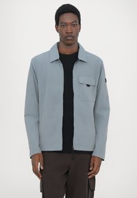 Grå zip-up jakke med krave og én brystlomme, lavet af glat stof. Afbalanceret design med en afslappet pasform og lange ærmer.