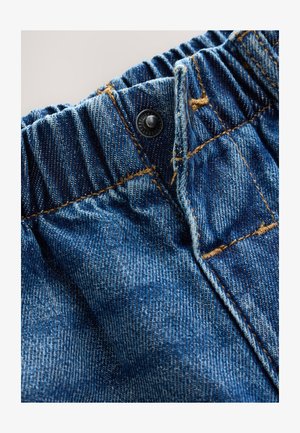 Close-up van denimstof met een geplooide tailleband, blauwe kleur, koperen knoop en gouden stiksel details.