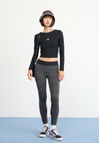 Top corto negro de canalé con logo en forma de corazón, leggings de tiro alto con patrón en negro y gris, calcetines blancos y zapatillas negras con acentos morados.