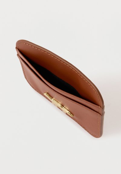 Καφέ δερμάτινο πορτοφόλι με λεία υφή, που διαθέτει χρυσό κούμπωμα και δύο θήκες, προσανατολισμένο προς τα πάνω σε απλό φόντο.