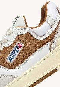 Sneaker in suede bianco e marrone con finitura testurizzata, caratterizzata da una patch logo cucita, lacci piatti e suola in gomma color crema.