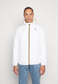 Giacca a vento bianca con chiusura a zip, dotata di cappuccio foderato in pelliccia e strisce di accento arancione/giallo lungo la parte frontale. Design leggero e casual.