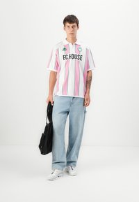 Biała koszulka polo w różowe pionowe paski, z zielonymi akcentami i napisem "F.C.HOUSE". Nosić z jasnoniebieskimi spodniami typu wide-leg i czarną torbą.