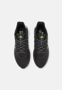 Zapatillas deportivas negras con acentos y cordones grises. Parte superior de material suave y suela de goma. Detalles en verde neón en el talón y la lengüeta.