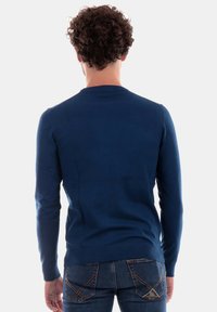 Maglione blu navy con maniche lunghe, scollo a giro e una trama in maglia liscia, abbinato a jeans in denim aderenti con cuciture in contrasto.