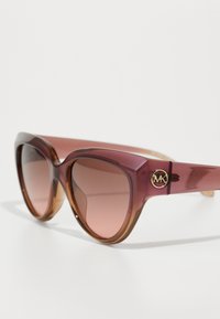 Óculos de sol em formato de gato com gradiente de cor ameixa para âmbar, apresentando um detalhe com logotipo dourado na armação e lentes com tonalidade.