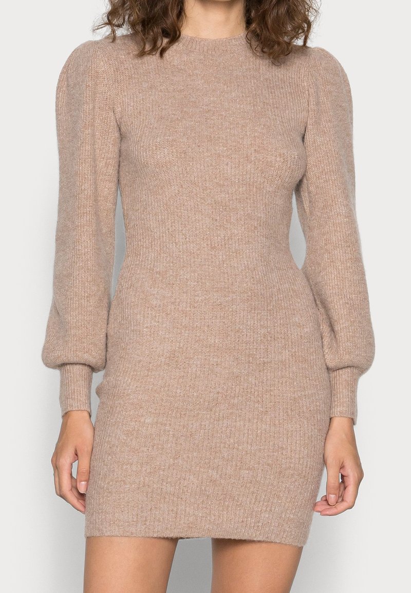 Robe mini en maille de couleur beige douce, dotée de manches longues bouffantes, d'une texture côtelée et d'une silhouette ajustée qui met en valeur la forme.