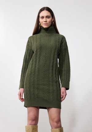 Strickkleid in olivgrün mit hohem Kragen, langen Ärmeln und strukturierten Zopfmustern. Der Saum endet knapp über dem Knie.
