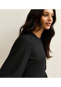 Top negro texturizado de manga larga con hombros abullonados y escote redondo, que presenta un patrón de canalé.