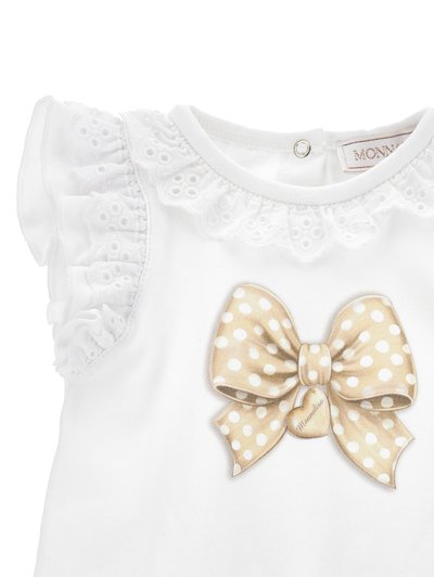Haut en coton blanc avec des manches en dentelle froncées, un grand nœud graphique en pois beige et une fermeture à boutons au dos.
