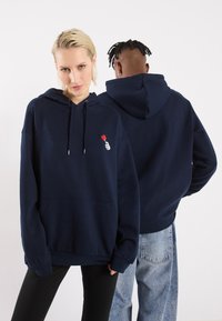 Σκούρο μπλε φούτερ από μαλακό υλικό, διαθέτει μπροστινή τσέπη, ρυθμιζόμενο κορδόνι και μικρή γραφική μορφή καρδιάς. Χαλαρή εφαρμογή.