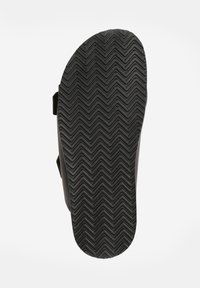 Semelle de sandal en caoutchouc noir avec un motif de rainures en zigzag, dotée d'une arche pour le soutien et d'une forme arrondie. Pas de marque ni d'accents visibles.