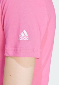Pink cotton t-shirt with short sleeves, featuring a white embroidered Adidas logo on the left sleeve. Even texture with minimal detailing.