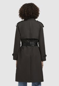 Trench coat negru cu curea, design dublu-breasted, epauleți pe umeri și accente cu butoane, fabricat dintr-un material neted și durabil.