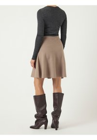 Haut à manches longues gris foncé associé à une jupe évasée couleur beige. Porté avec des bottes en cuir marron montant jusqu'aux genoux, à talon aiguille.